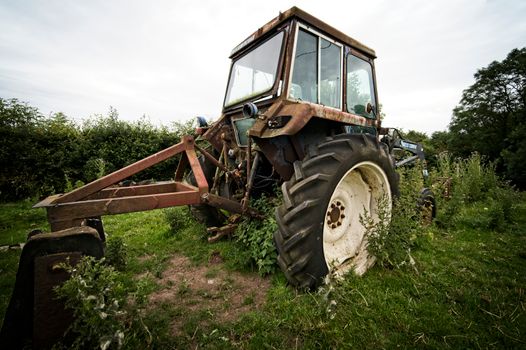 An old, rusted tractor overgrown with weeds in the English countryside.