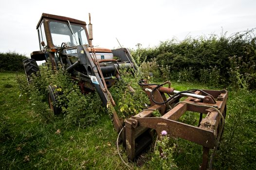 An old, overgrown tractor sits unused in a lush green field in England.