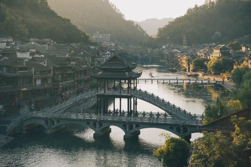 Free A serene sunset view over Fenghuang Ancient Town's iconic bridge and river scene. Stock Photo