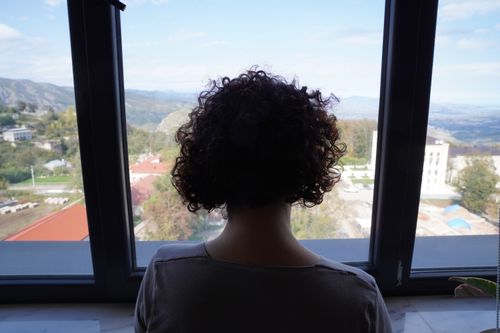 Free A woman with curly hair gazing out a window at a scenic mountain view, indoors. Stock Photo