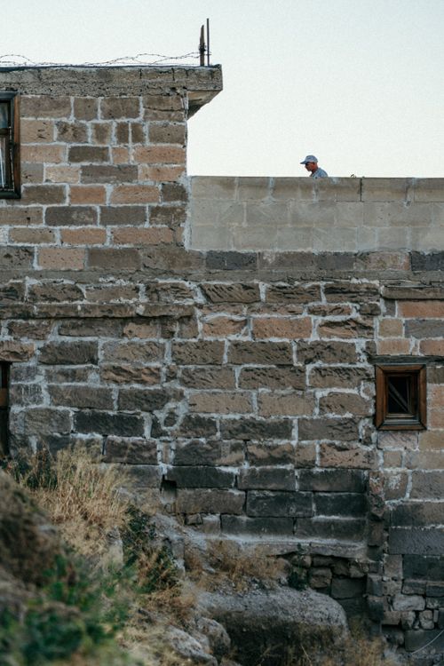 Free A person wearing a cap peers over a stone wall of a historic building during the day. Stock Photo