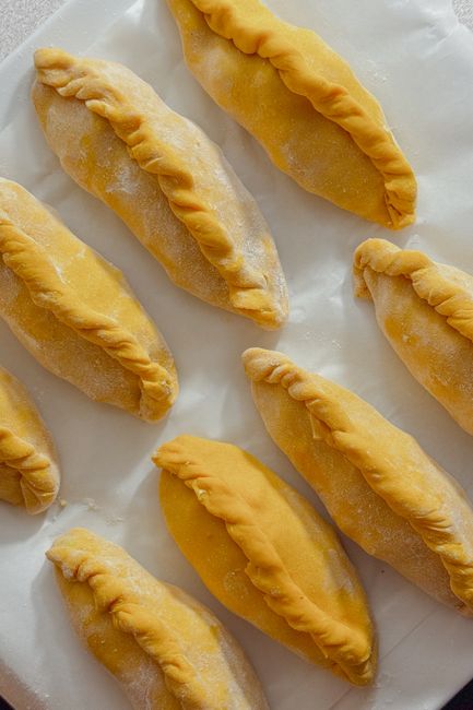 Golden homemade empanadas lined up on a baking sheet, ready for baking.