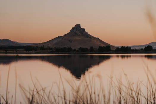 A serene view of a mountain reflecting in a calm lake during a vibrant sunset, creating a peaceful natural landscape.