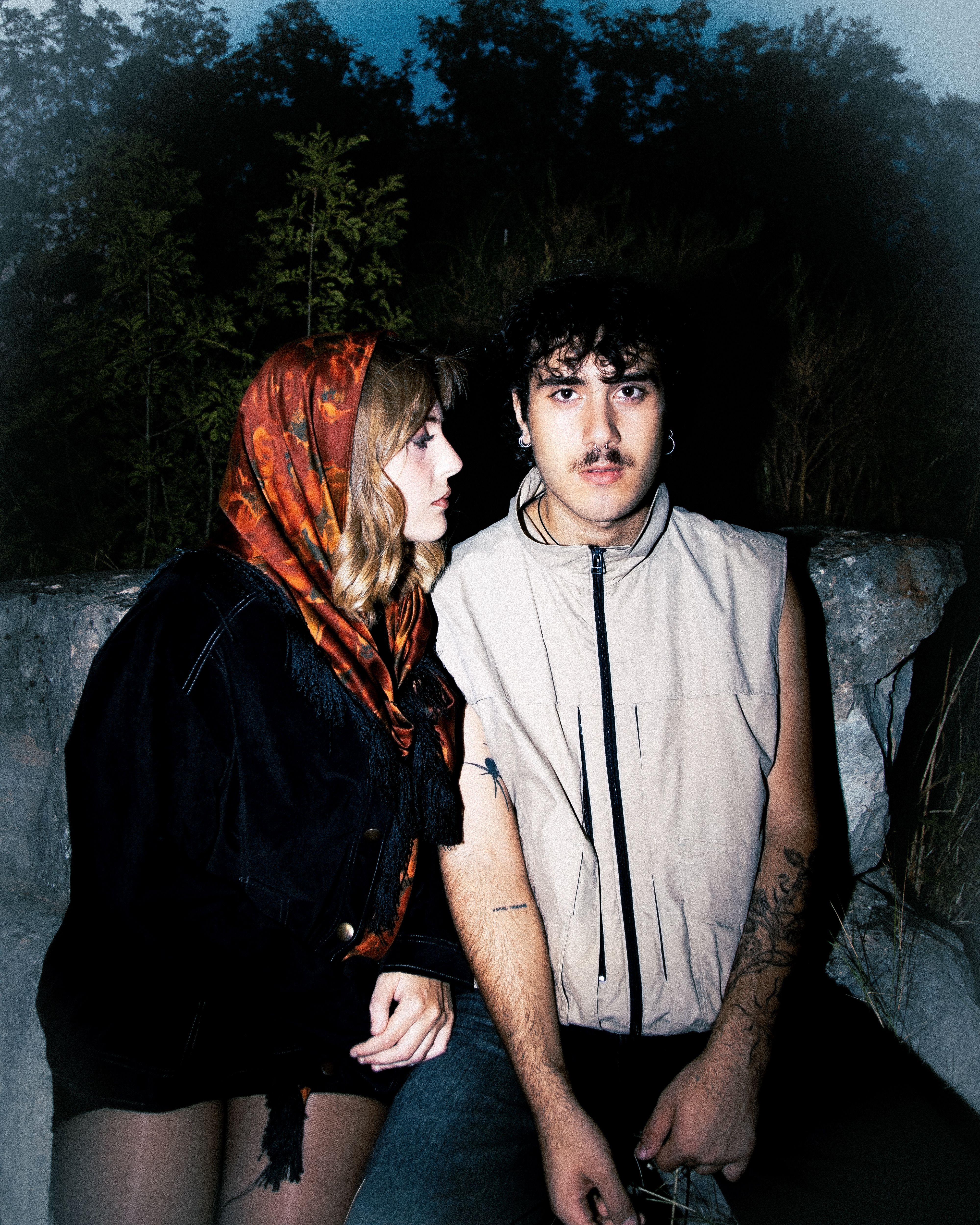 Portrait of a couple with alternative style seated outdoors at night, embodying grunge fashion.
