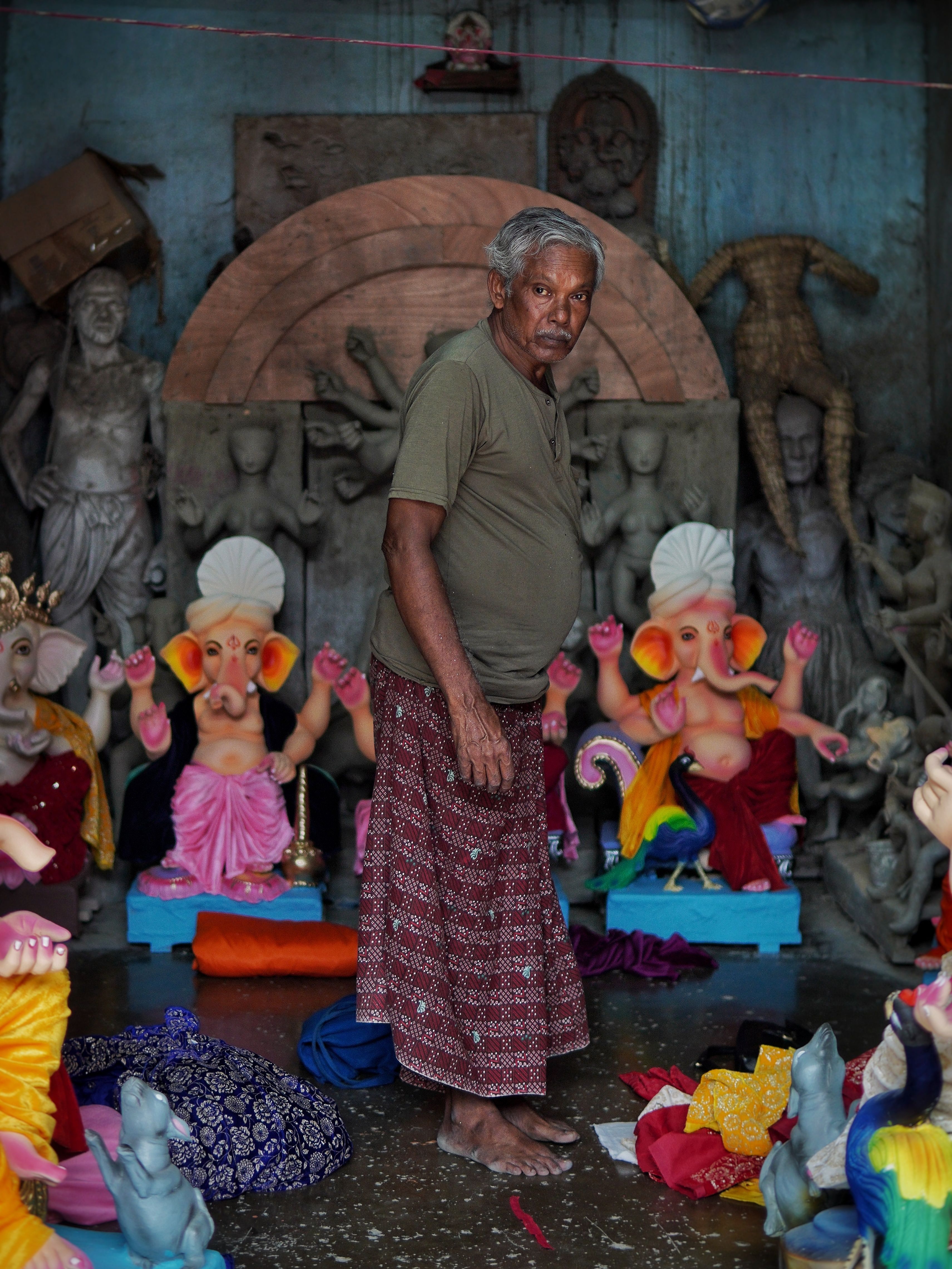 An artisan in Kolkata works amidst vivid Ganesha idols, showcasing traditional craftsmanship.