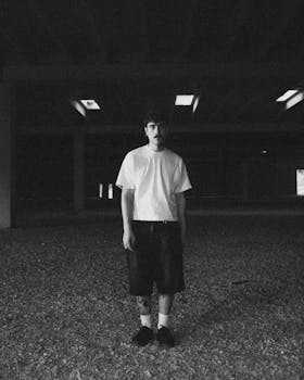 Moody black and white portrait of a man in a dark urban setting.