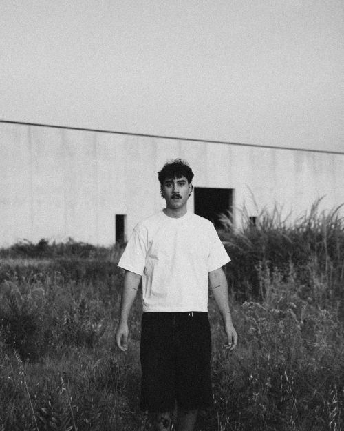 Free A young man stands in front of industrial building in moody black and white. Stock Photo