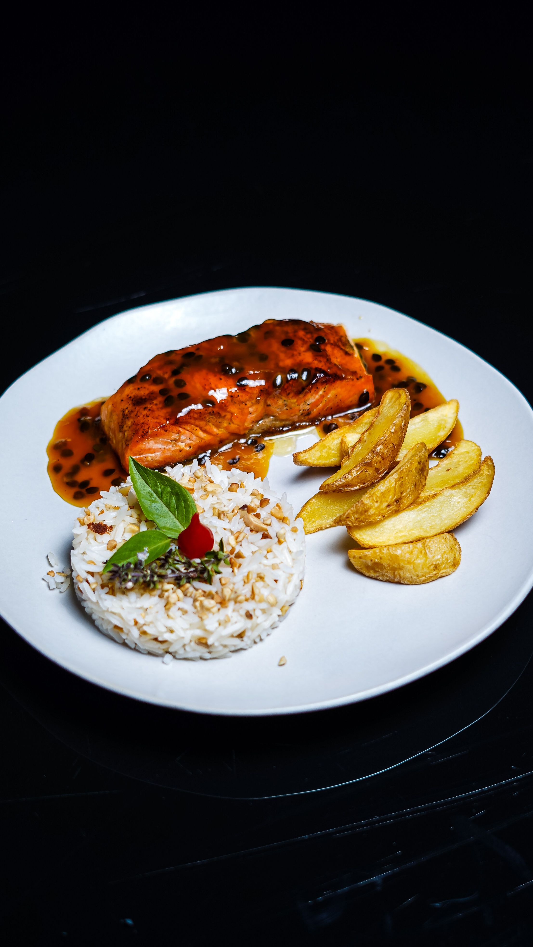 A gourmet dish featuring glazed salmon, seasoned rice, and golden potato wedges.