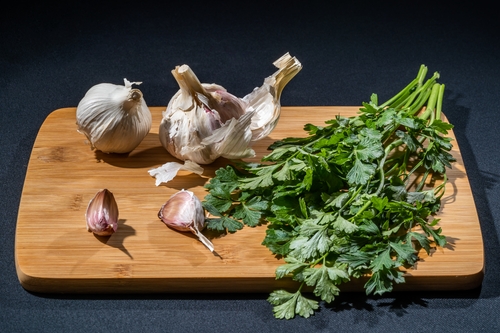 Free Fresh garlic bulbs and parsley leaves arranged on a wooden cutting board, perfect for culinary and cooking stock images. Stock Photo