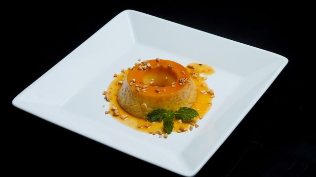 A beautifully plated caramel flan with mint leaves and nuts, set against a black background.