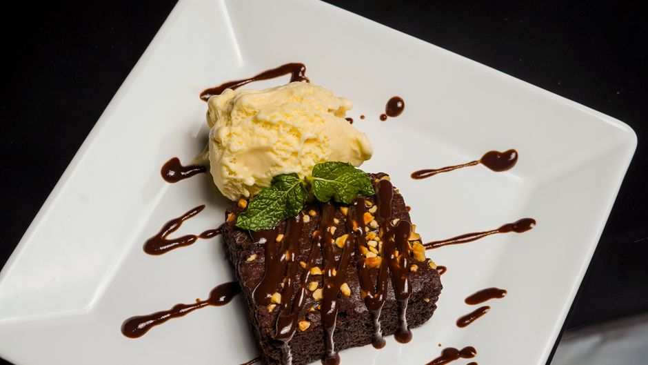 A dish of dark, glossy brownie pudding with a cracked cakey top and a molten, pudding-like center, scooped and topped with a melting scoop of vanilla ice cream.
