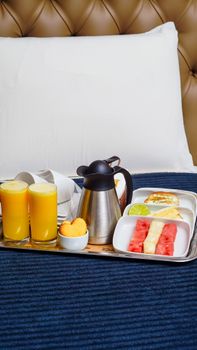 Elegant breakfast tray with fresh juice and fruits on a cozy bed setting.