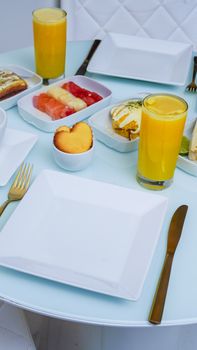 Stylish breakfast table with fresh juices, a variety of fruits, and pastries on white plates.