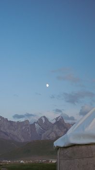 A yurt set against a mountain range under the moonlight, capturing a serene landscape.