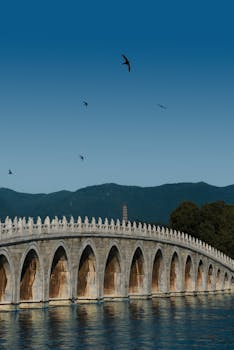 Majestic stone bridge arches gracefully over calm water with distant mountains.