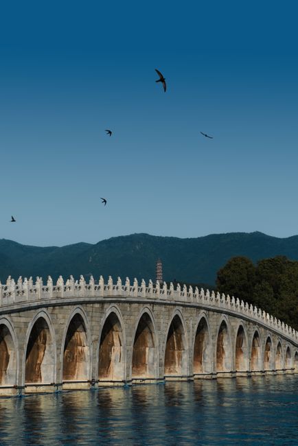 Majestic stone bridge arches gracefully over calm water with distant mountains.