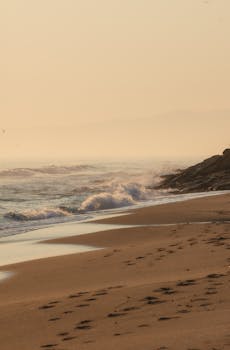 Peaceful waves at sunset on a sandy beach with footprints in the sand.