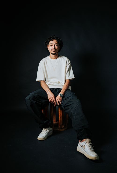 Free Stylish young man in streetwear clothing posing confidently in a studio with a dark background. Stock Photo