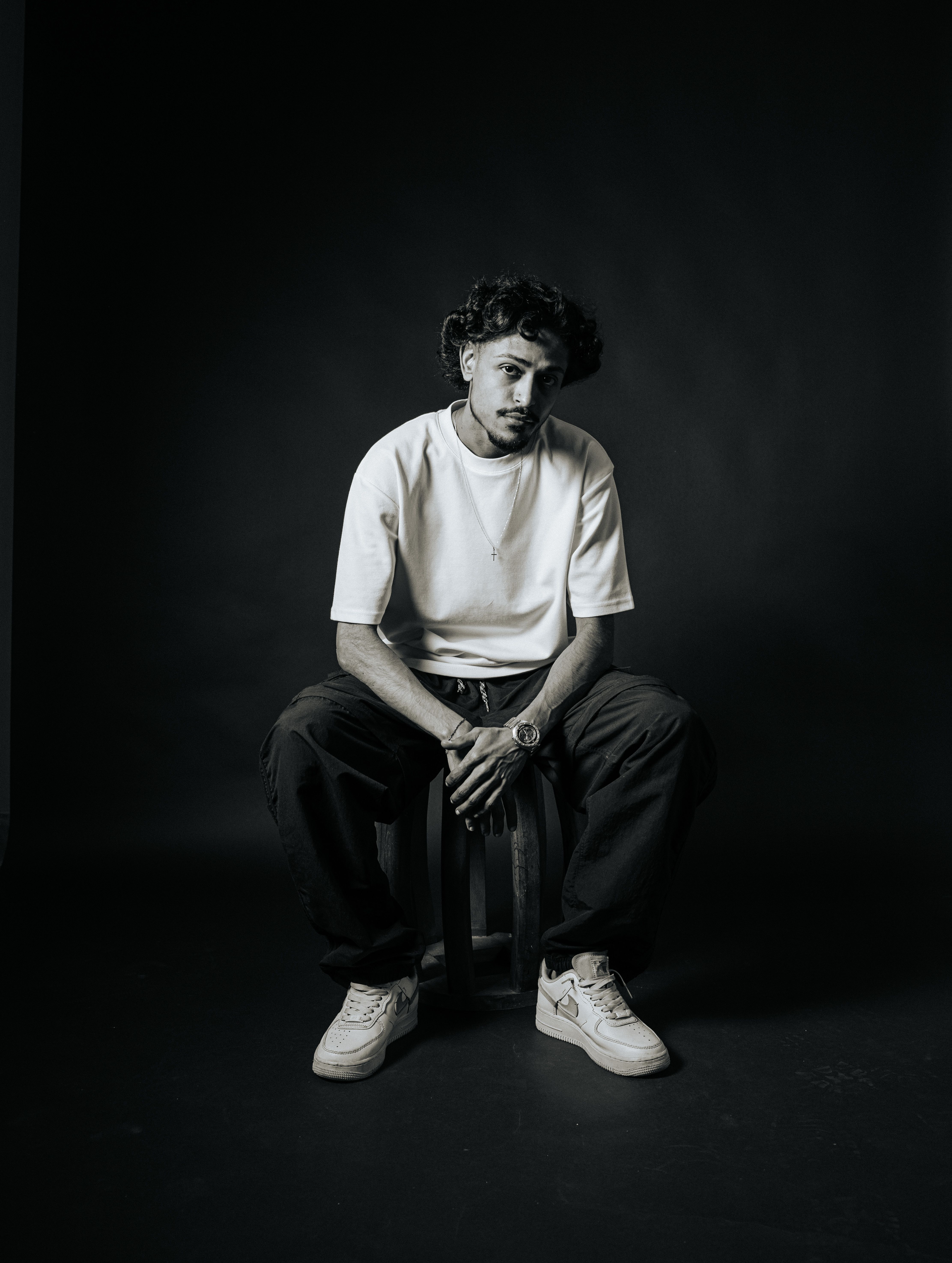 Black and white portrait of a fashionable man seated in a studio setting, exuding a modern and edgy vibe.