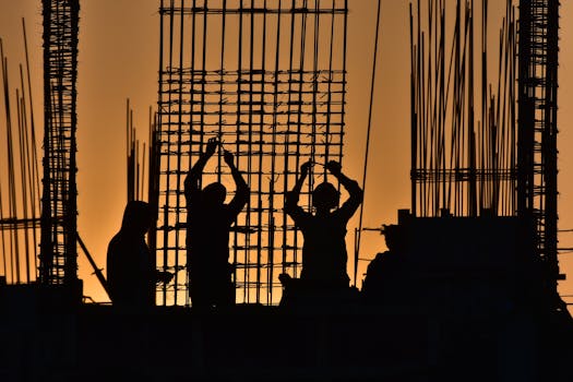 Silhouetted construction workers at a site during sunset, creating a dramatic scene.