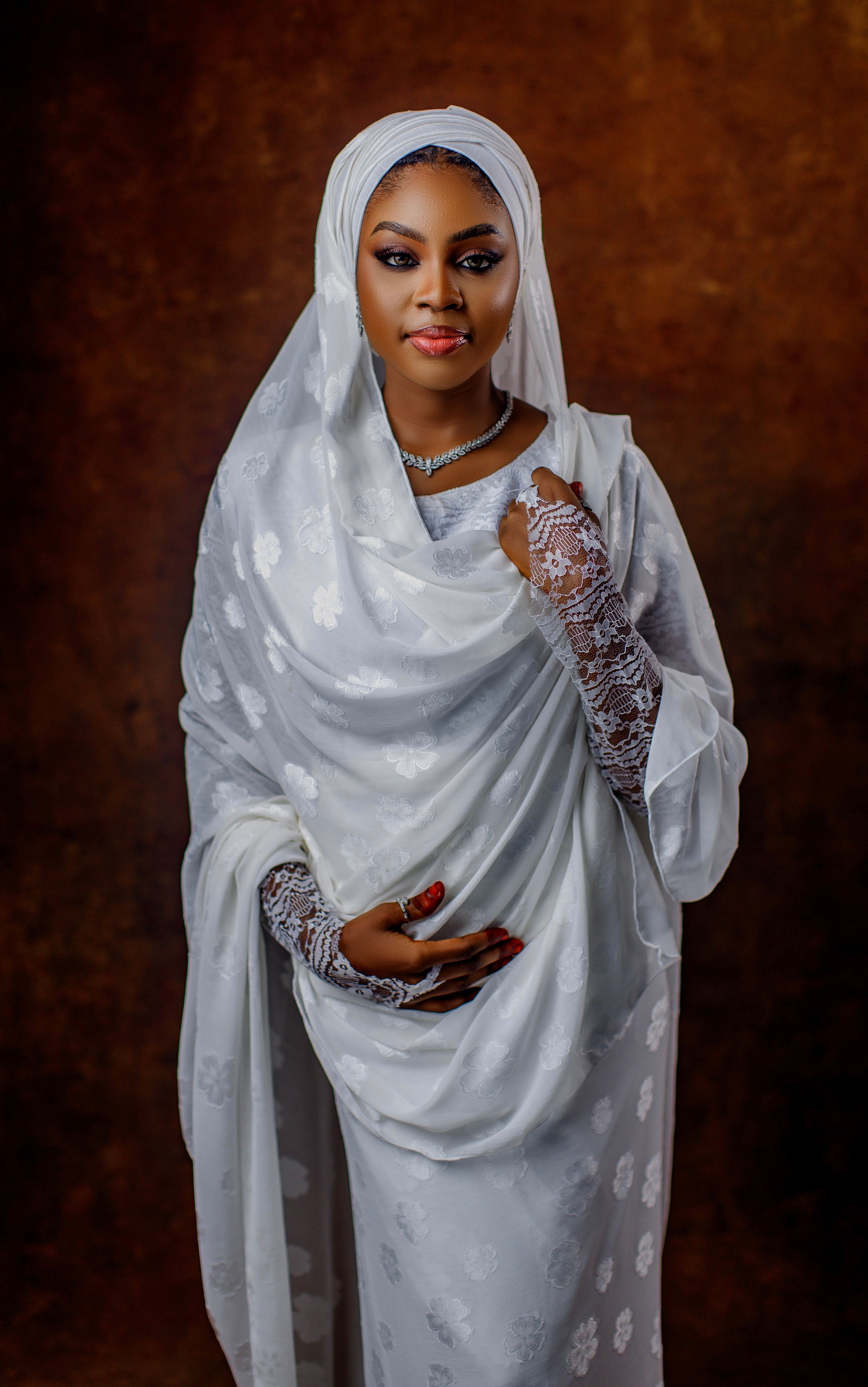 Portrait of a woman in elegant traditional white attire with lace details, set against a warm backdrop.