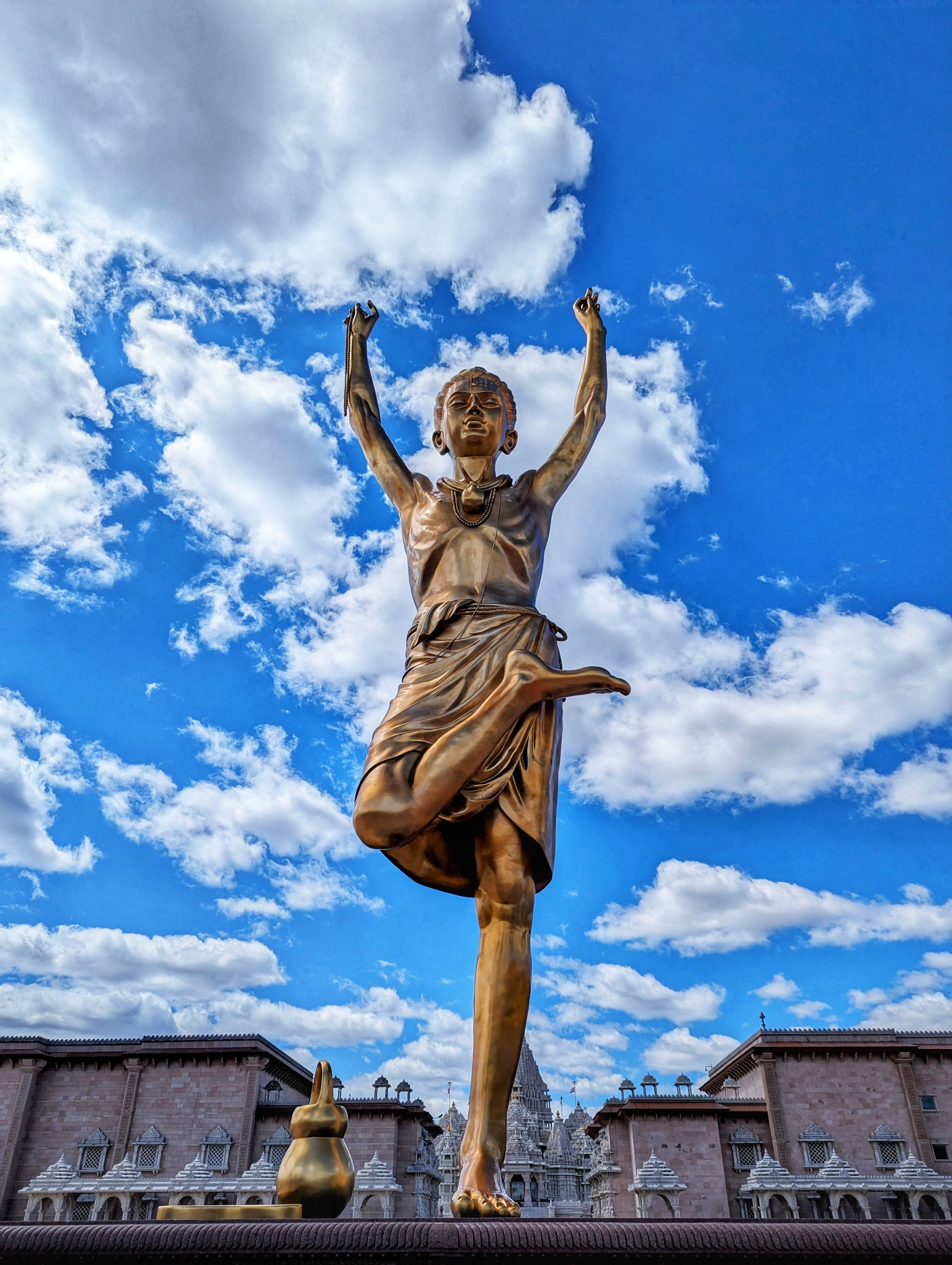 Dramatic statue reaching skyward set against a vibrant blue sky with clouds, creating a dynamic urban landscape.
