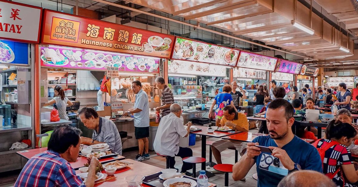 A lively hawker center in Singapore with people eating and talking, colorful food stalls