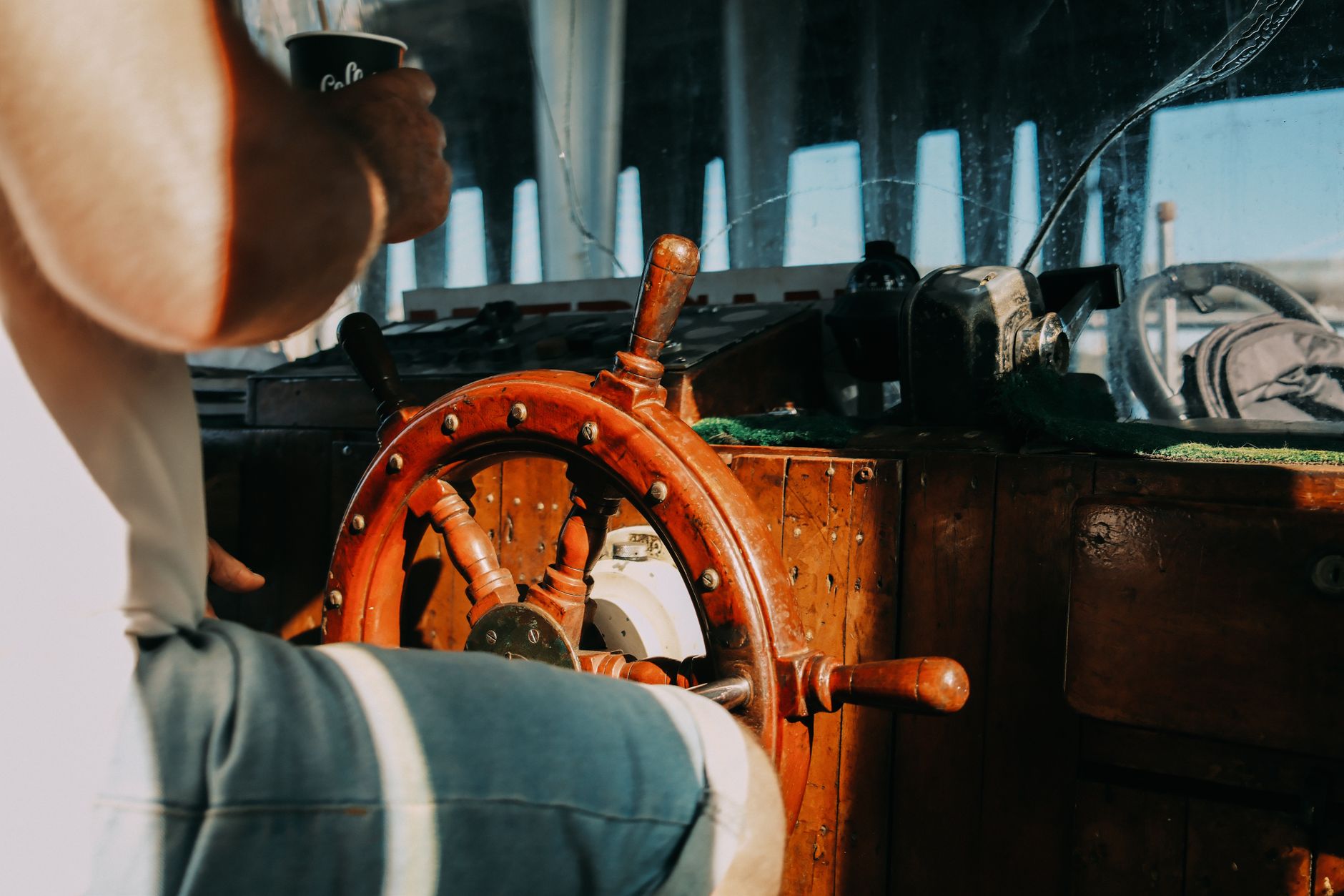 A man steering a boat using a classic wooden helm in natural daylight.
