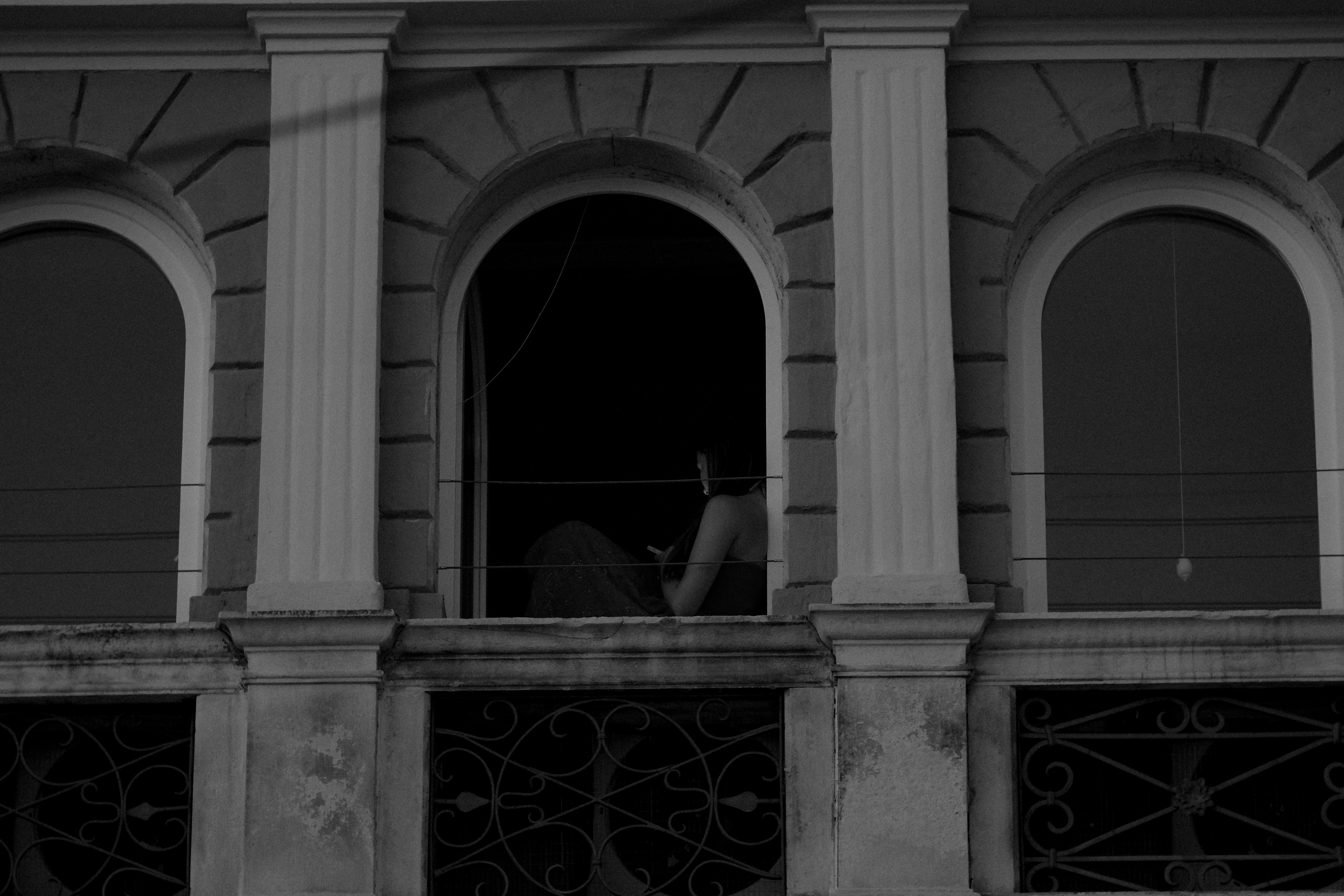 Free Black and white photo of a woman sitting in a window with architectural details in Croatia. Stock Photo