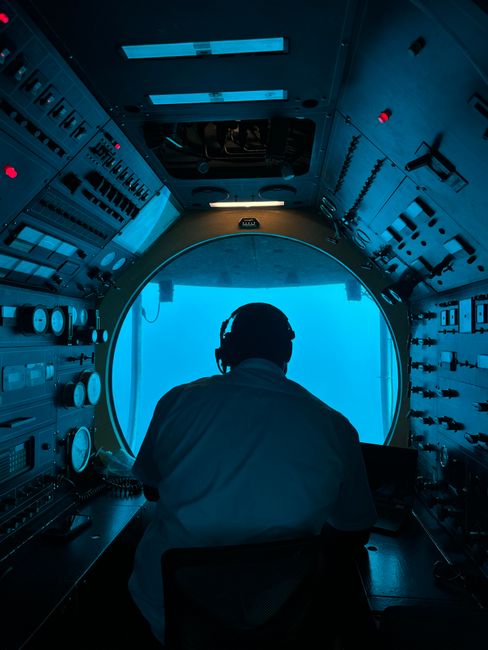 Operator in submarine control room analyzing equipment and blue ocean view.
