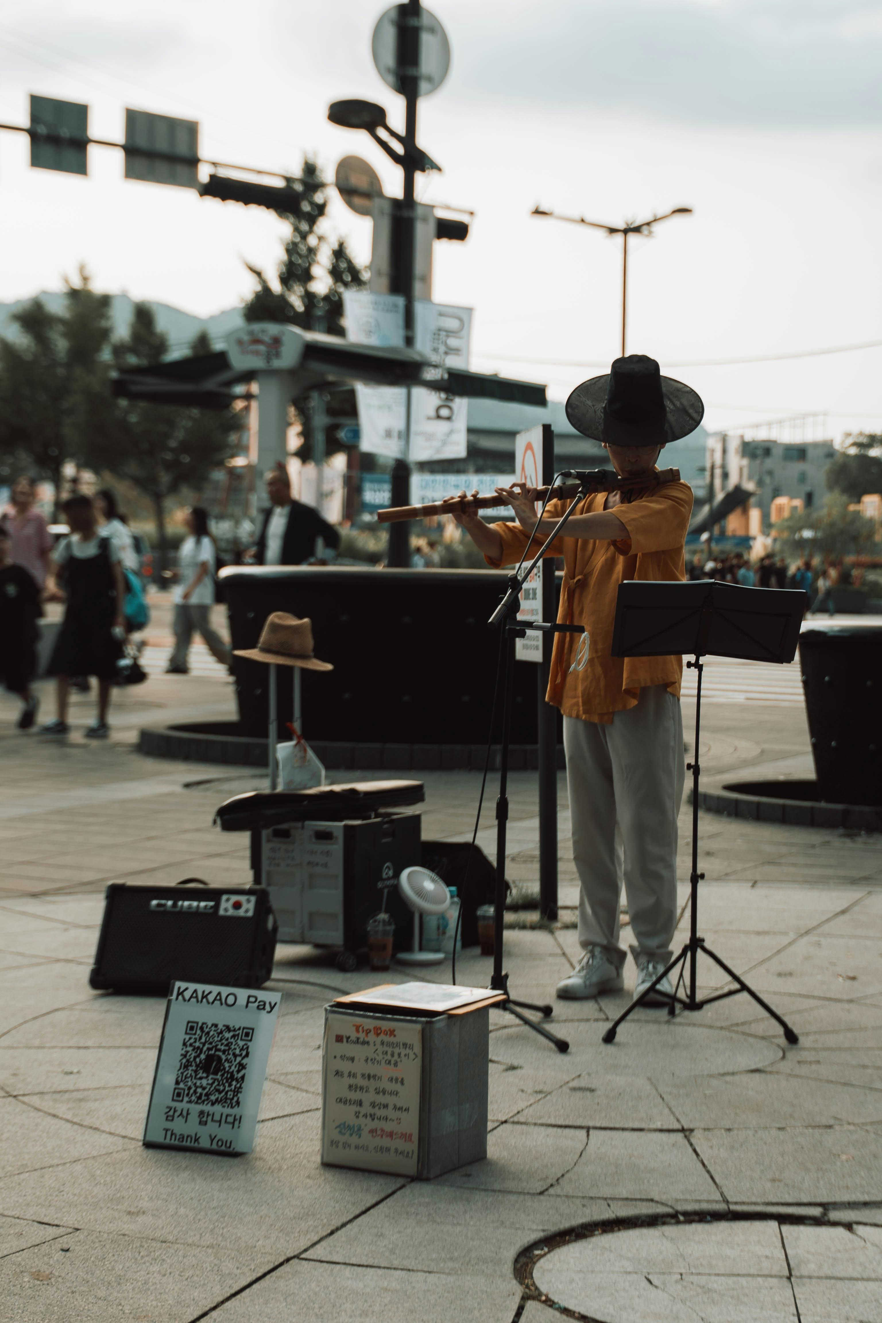 Street performer in traditional attire playing a flute in a bustling Korean city.