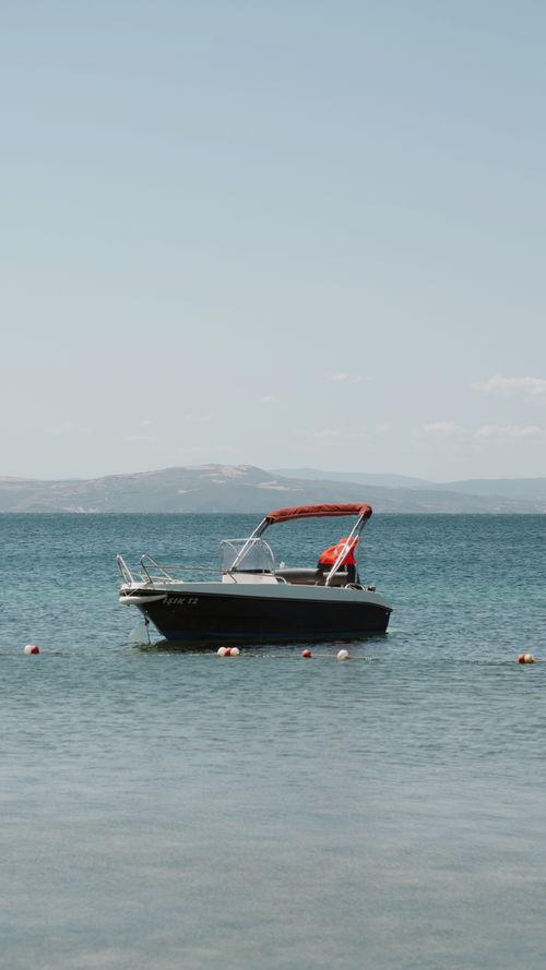 Free A small motorboat gently floats on a clear blue sea under a bright sky, ideal for travel and leisure. Stock Photo