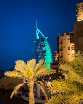 Captured evening view of Burj Al Arab in Dubai, a landmark of modern architecture with palm trees foreground.