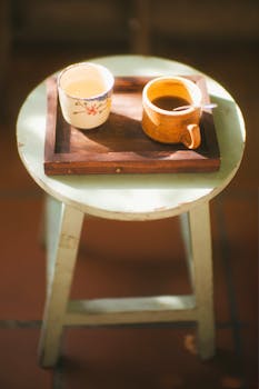 Two rustic coffee cups on a wooden tray, set on a vintage stool in warm sunlight.