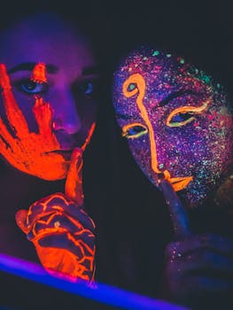 这幅引人注目的肖像拍摄于夜间，描绘了两个涂着霓虹灯脸的女人，在黑暗中闪闪发光