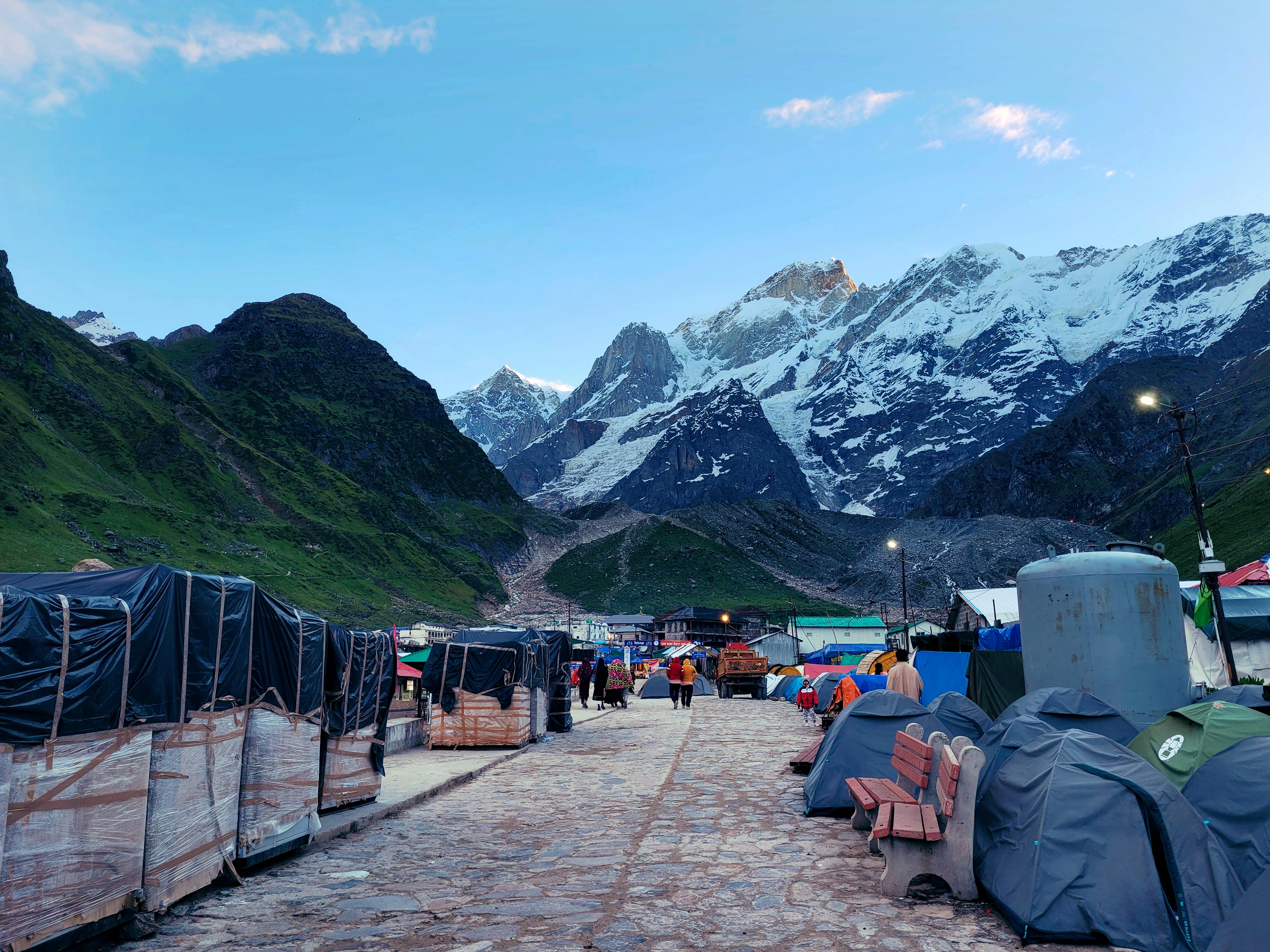 Picturesque Kedarnath setting with majestic snow-covered mountains and tents along a pathway. - Mawlynnong