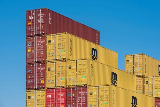 Colorful shipping containers stacked high under a clear blue sky, displaying industrial logistics.