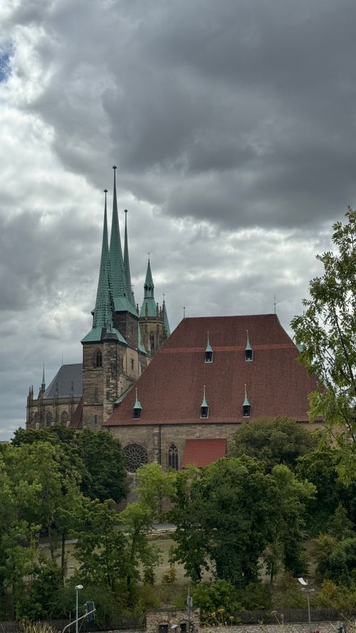 Free A majestic Gothic cathedral with spires under a cloudy sky, surrounded by greenery. Stock Photo