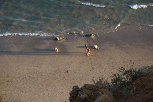 Free Aerial shot of a couple walking on a sandy beach during sunset with gentle waves. Stock Photo