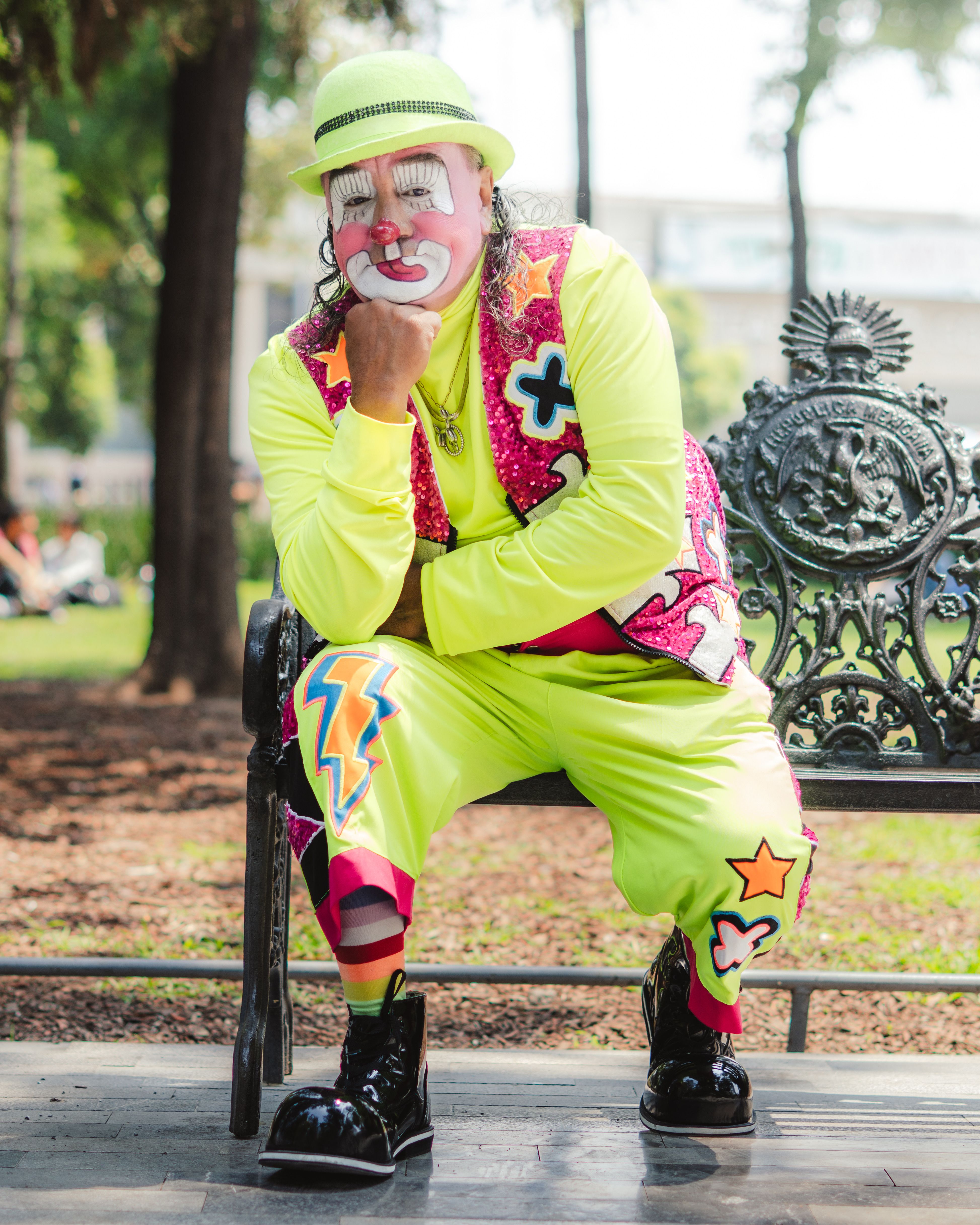 Vibrant clown sitting on a park bench in Mexico City, showcasing lively street art fashion.