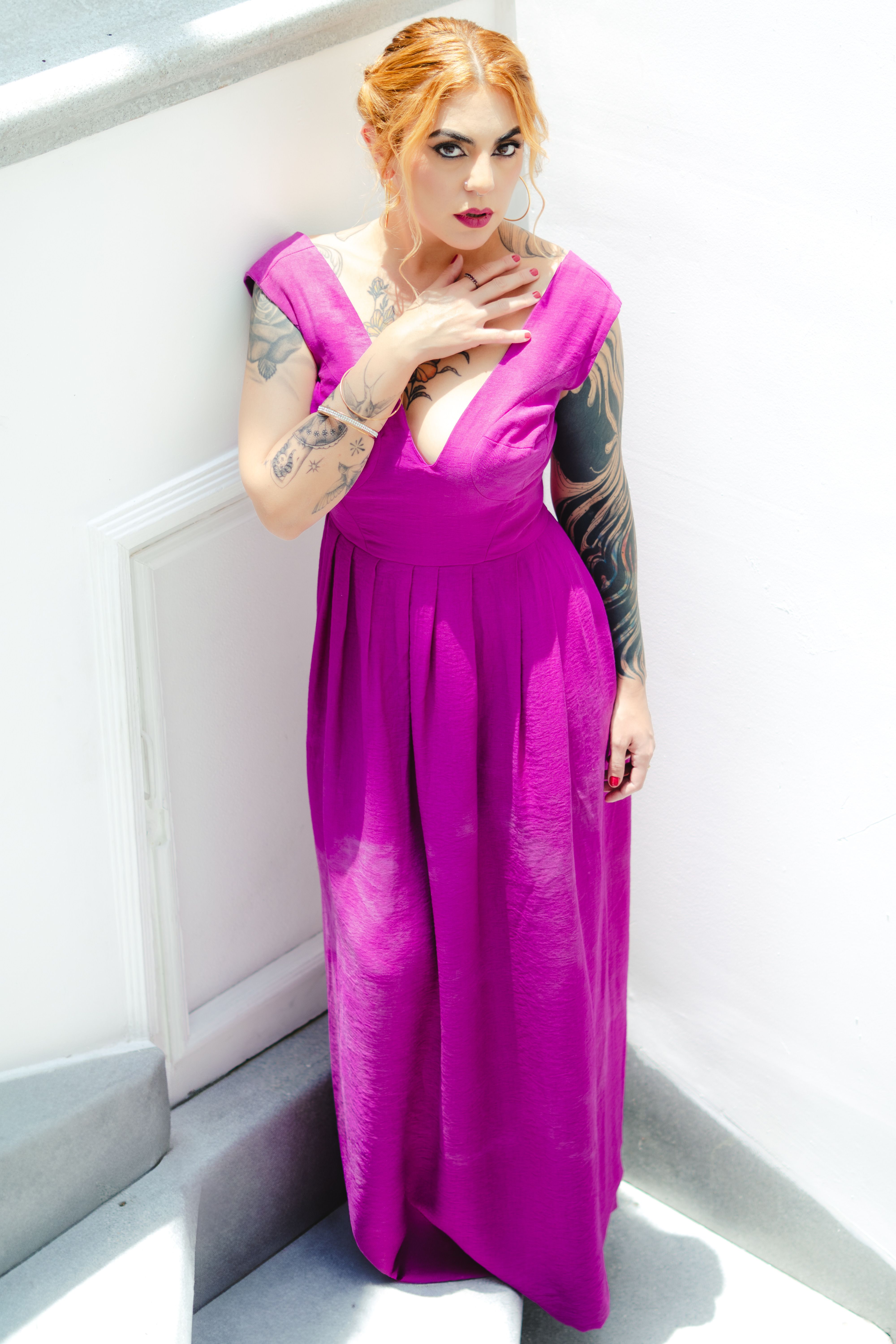 Stylish adult woman in vibrant pink dress with tattoos posing indoors in Mexico City.