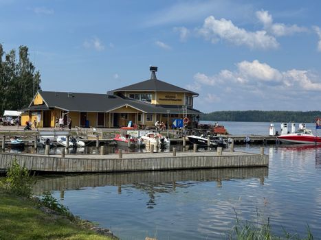 Bright summer view of marina with boats and a yellow building by the lake.