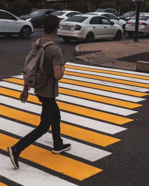 Free Man crossing city street on zebra crossing with traffic in background. Stock Photo