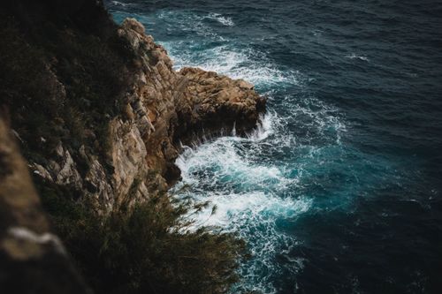 Free A powerful view of waves crashing against the rocky cliffs of Dubrovnik's coastline under a moody sky. Stock Photo