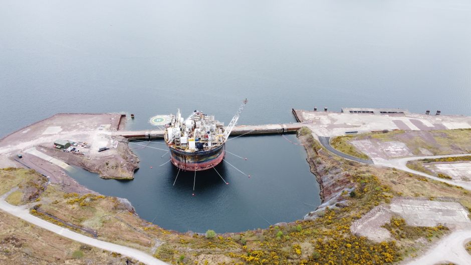 Aerial view of an oil rig docked in a Scottish loch surrounded by rugged landscape.