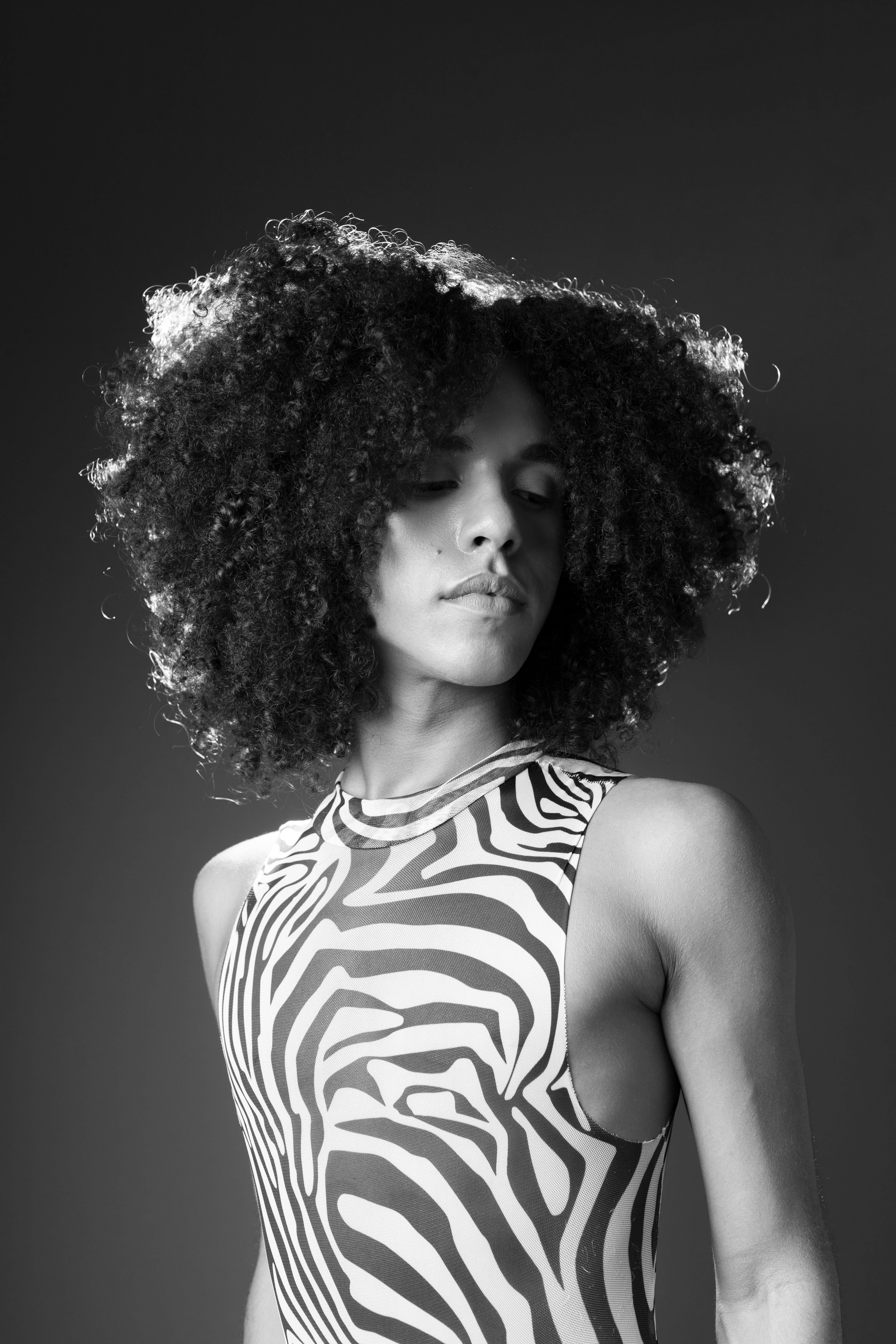 Artistic black and white portrait of a person in a zebra print dress, showcasing natural curly hair.