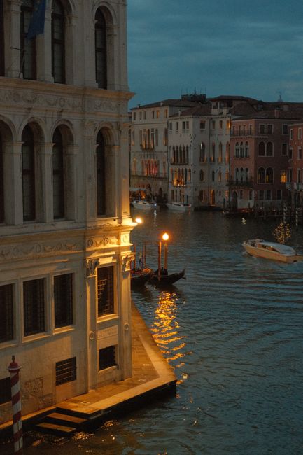 Scenic view of a Venetian canal at dusk, featuring gondolas and historic architecture.