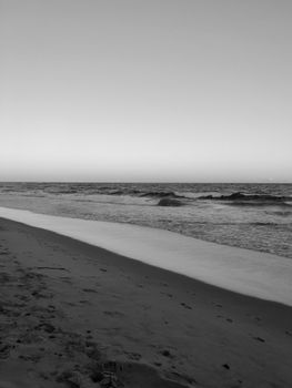 A tranquil beach with gentle waves in black and white, captured at sunset.