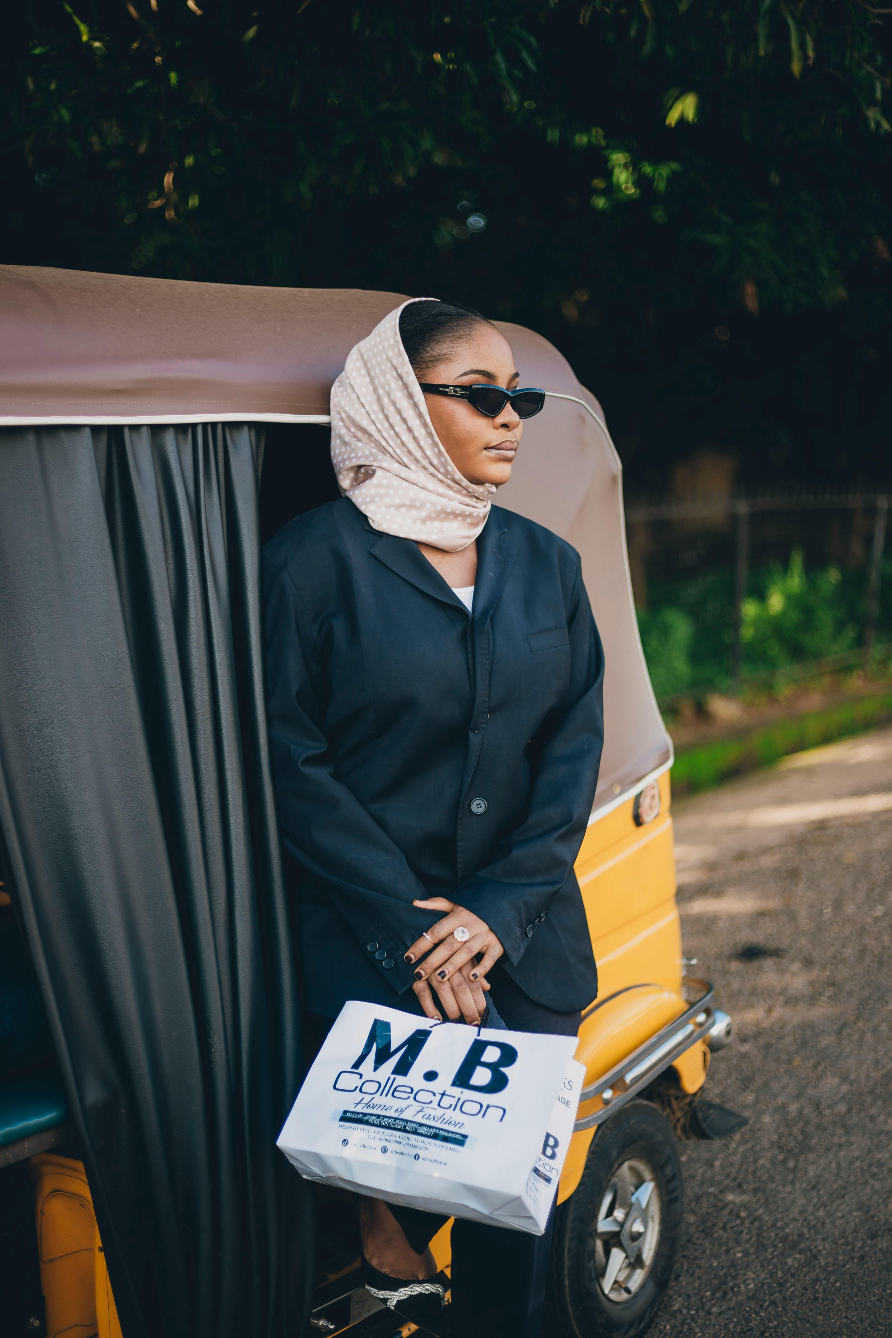 Free Elegant woman in sunglasses and headscarf holding designer bag next to yellow tuk-tuk. Stock Photo