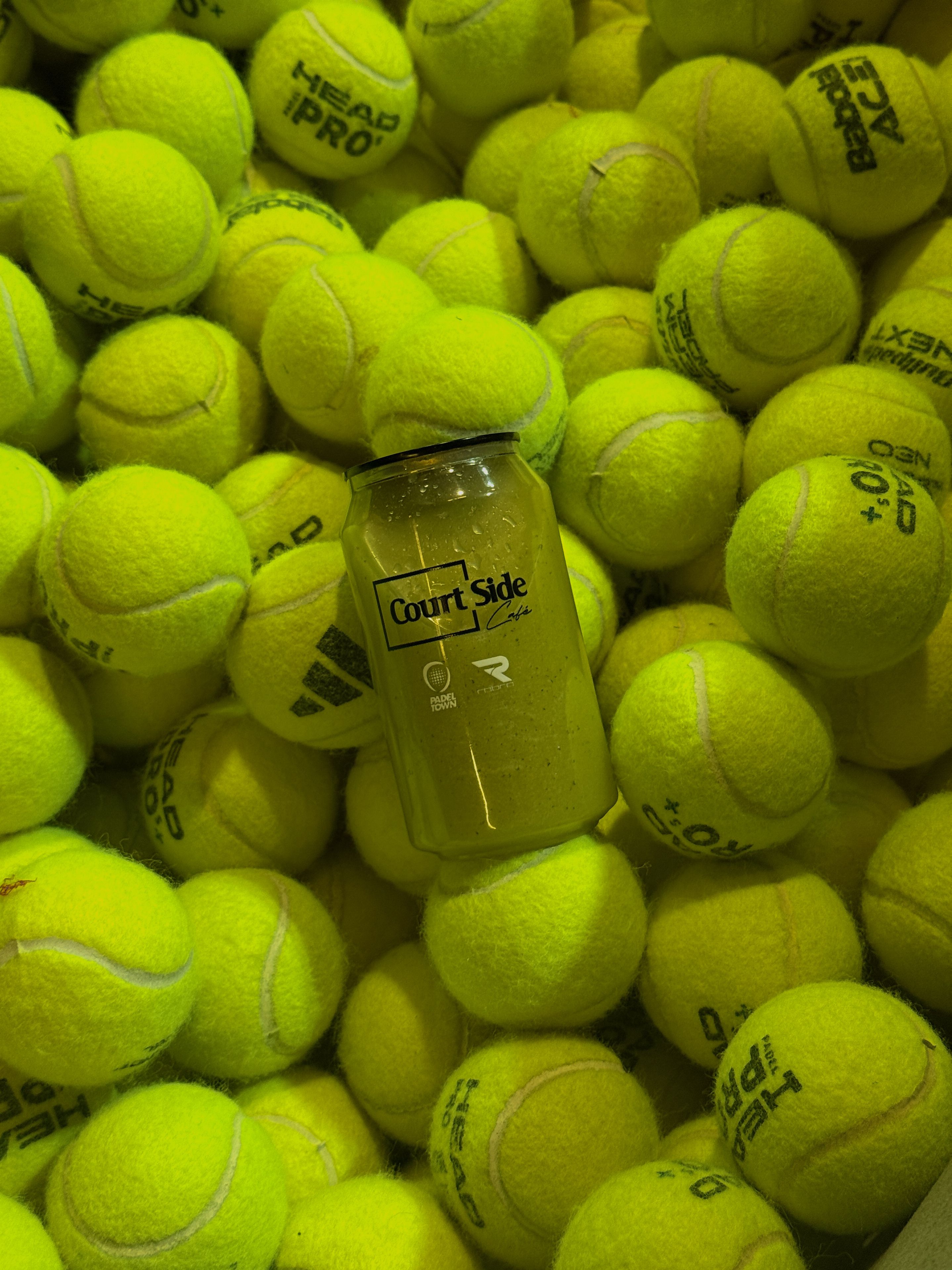 Pile of bright yellow tennis balls with a can of Court Side drink in the center.